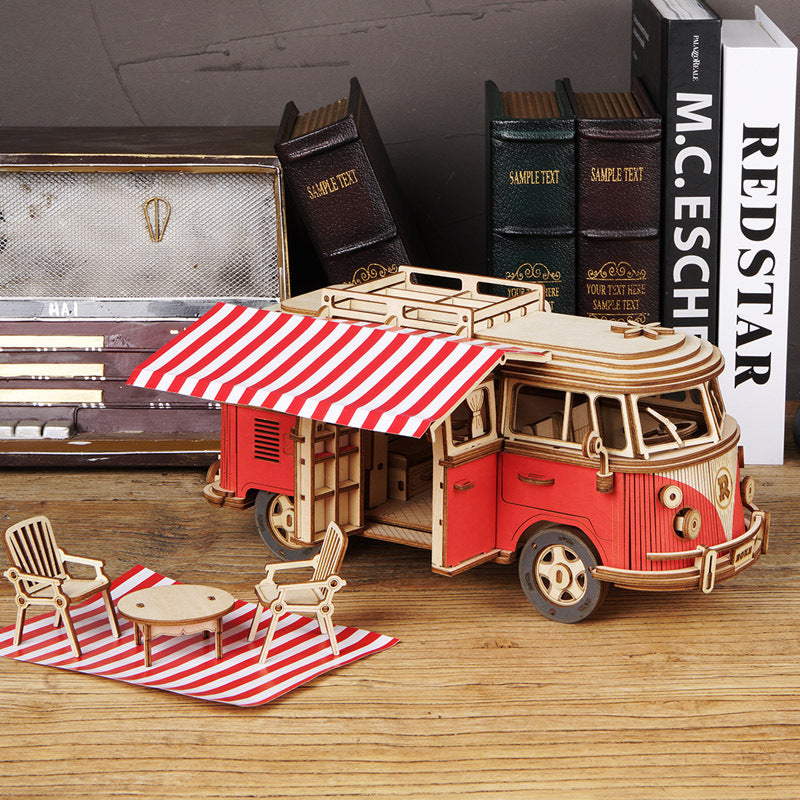 Wooden model of a red and beige van with a striped awning on a wooden surface.