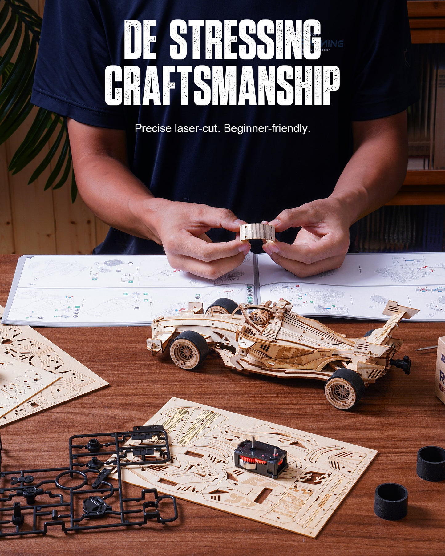 Person assembling a wooden model car kit with text 'De Stressing Craftsmanship' on a wooden table.
